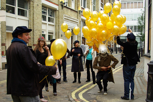 A man with a stag's head waits while people tie balloons to his antlers.